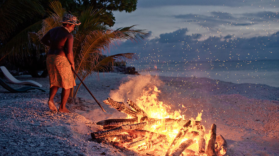 A man stoking a fire on the beach. Rangiroa. Credit: Hélène Havard / Tahiti Tourisme